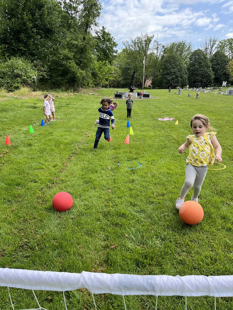 Children running and playing outside in an organized game with kickballs.